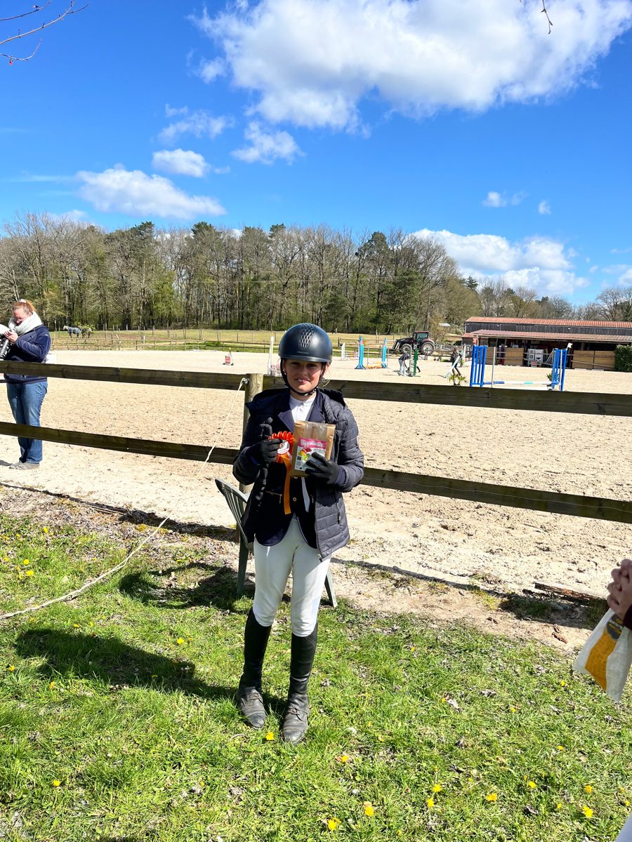 Jeune cavalière avec sa rosette et son lot après une compétition aux Écuries de Saint-Amand